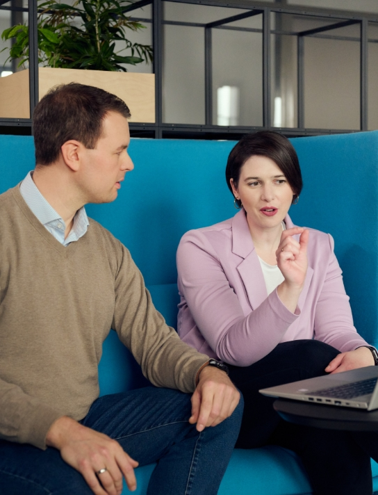 Zwei Personen besprechen auf einem Sofa etwas am Laptop